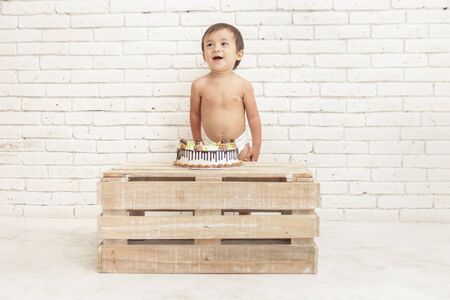 portait of cheerful adorable toddler with his cake on white walls backgroundの写真素材