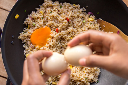 top view of human hands cracking egg for adding into fried riceの写真素材