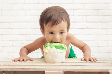 portrait of adorable handsome toddler eating sponge cake with white walls on backgroundの写真素材