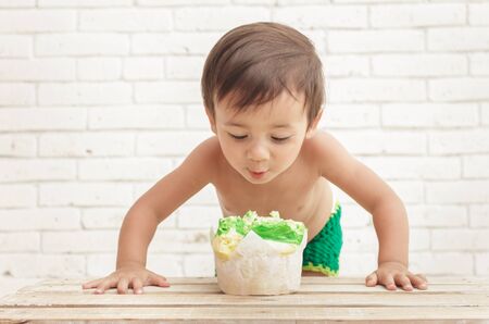 portrait of handsome toddler in astonishment looking at sponge cake with white walls on backgroundの写真素材