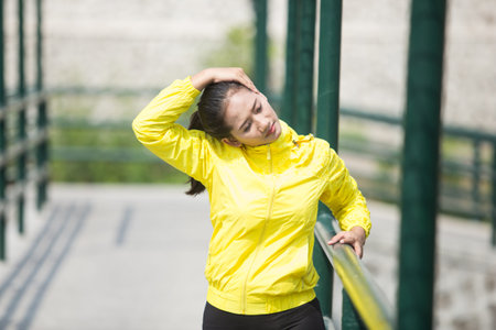 A portrait of a young asian woman exercising outdoor in yellow neon jacket, stretching