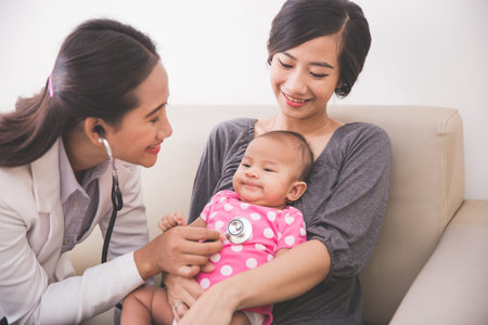 A portrait of an Asian female pediatrician examining a baby girl in the mother lap