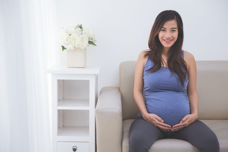 A portrait of beautiful pregnant woman smiling in to camera while sitting on a couch