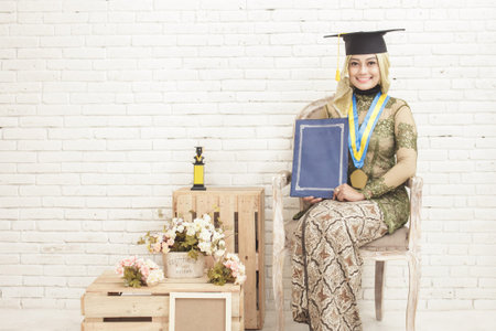 portrait of indonesia female graduated student wearing traditional clothes sitting at decorated room...