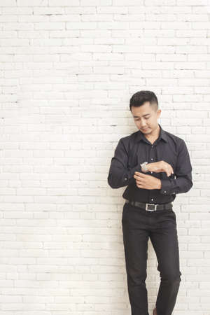 portrait of casual asian man standing while fixing his shirt sleeve at decorated room with white wall backgroundの写真素材