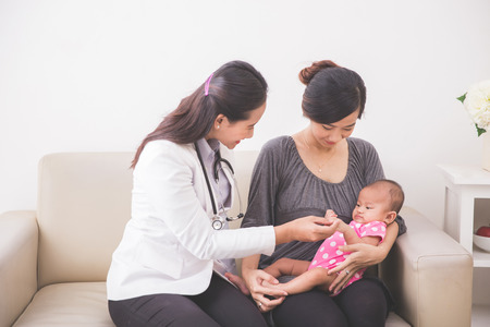 A portrait of an Asian female pediatrician examining a baby girl in the mother lapの写真素材