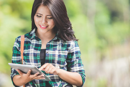 A portrait of a young asian woman using a tablet pc while  walking on the park