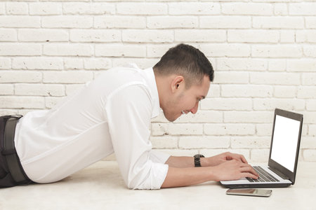 portrait of young businessman lying face down on the floor while working on laptopの写真素材