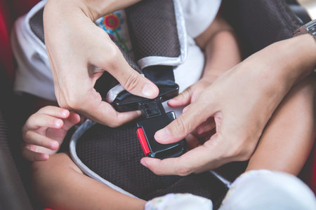 Protection in the car. Hands of  woman is fastening security belt to baby in car seat