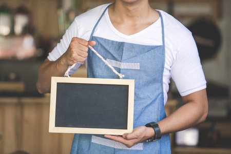 portrait of confident young asian male cafe owner standing with blank boardの写真素材