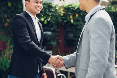 Two happy young men shaking hands in the rest area of the officeの写真素材