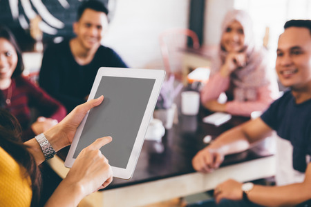 portrait of young woman holding tablet talking about something in the cafe with her friends. with clipping path on screenの写真素材