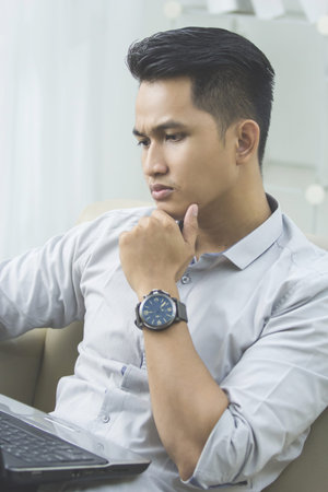 Image of young asian man sitting on sofa and using laptop