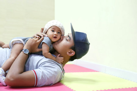 A portrait of a Young Asian father holding and kissing his adorable baby