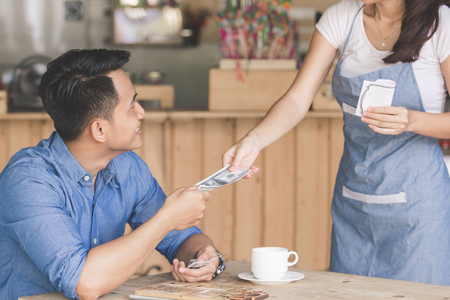 Smiling customer paying by cash at the coffee shopの写真素材