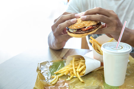 close up of a man having Hamburger served with french fries and soda in a restaurant