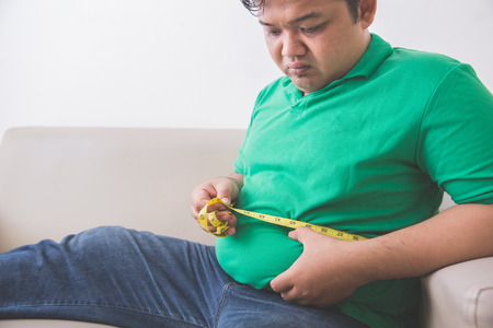 portrait of man measuring his belly at homeの写真素材
