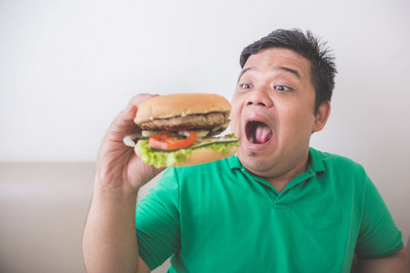 Portrait of Overweight man eating hamburger at home
