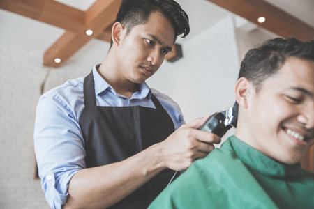 portrait of Young handsome barber making haircut of attractive man in barbershopの写真素材