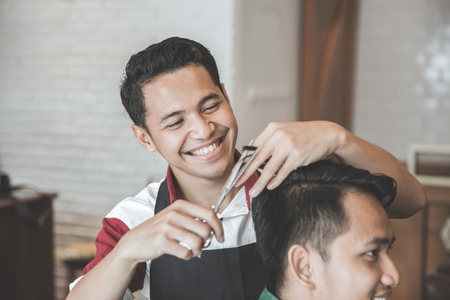 Cheerful young man getting haircut by hairdresser at barbershopの写真素材