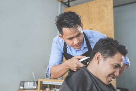 Cheerful young man getting haircut by hairdresser at barbershopの写真素材