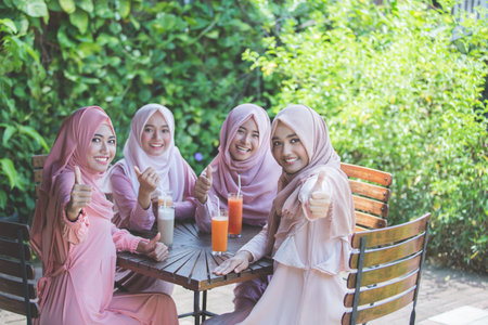 group of asian woman with hijab showing thumbs up to camera while sitting in cafe