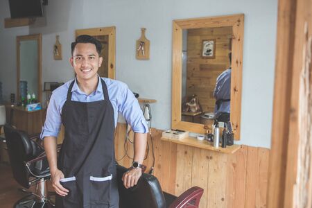Confident barber expert. Young man looking at camera and smiling standing at barbershopの写真素材