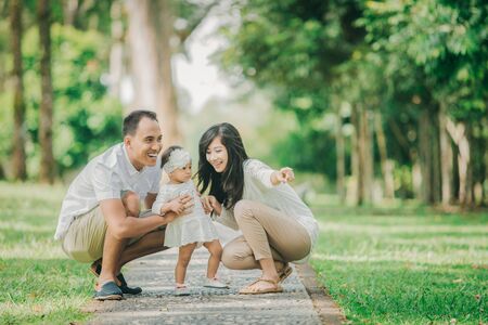 Beautiful Happy family together young parents in white clothes walking with their baby daughter in the park on a sunny summer day.の写真素材