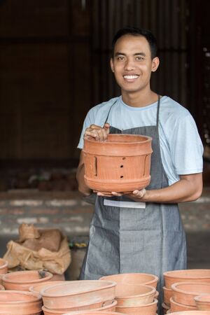 portrait of Smiling male potter holding his product in pottery workshopの写真素材