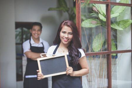 portrait of waitress standing at the front of a cafe inviting people to come inの写真素材