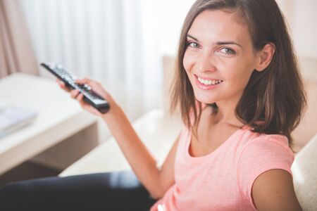 beautiful woman relaxing in living room holding remote control and watching television or tvの写真素材