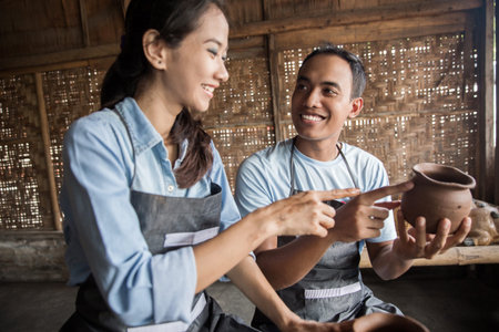 Portrait of male potter assisting female potter in pottery workshop