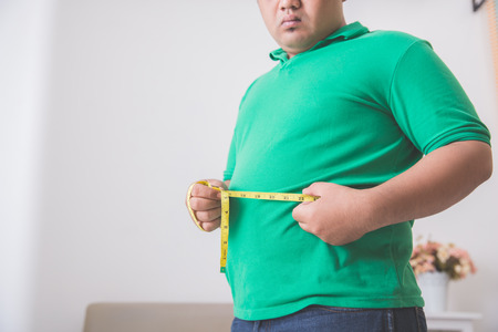 close up portrait of overweight man measuring his belly at homeの写真素材