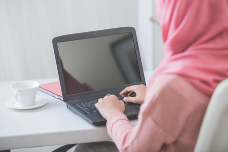 portrait of a woman with hijab using laptop at home. shotting from behindの写真素材