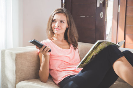 woman relaxing in living room holding remote control and watching television or tv