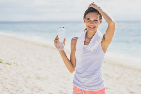 portrait of happy sporty girl holding a bottle of mineral water for refreshment at the beachの写真素材