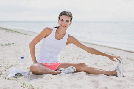 portrait of happy healthy woman smiling while doing leg stretching at the beach