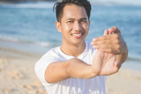 handsome asian athlete warming up before jogging at the beachの写真素材