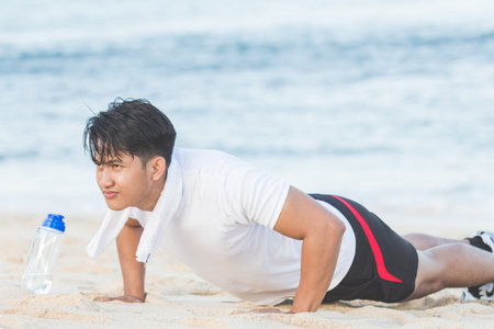 Young man doing push-ups outdoors at the beach