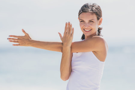 portrait of sporty woman smiling while doing arms stretching