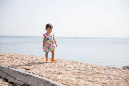 happy young baby girl walking with beautiful dress in the sidewalk at the beachの写真素材