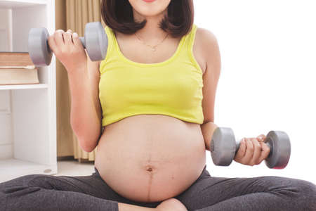 portrait of pregnant woman exercising using dumbbells, close up to her stomachの写真素材