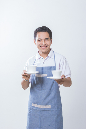 Small business shop owner. Apron man smiling proud and happy isolated on white background. Young entrepreneur asian male with two cup of coffeeの写真素材