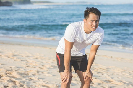 Young sport man taking a break during a challenging jogging at the beach