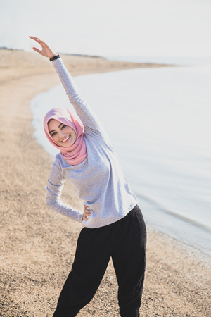 portrait of beautiful woman wearing hijab doing body stretching at the beachの写真素材