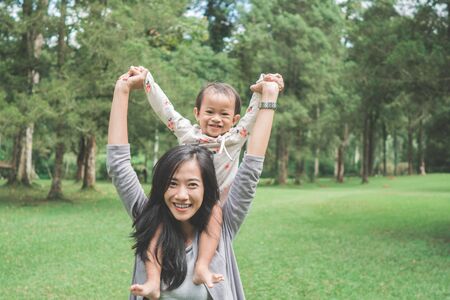 portrait of happy baby girl sitting on mom's shoulder in the parkの写真素材