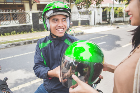 portrait of happy commercial motorcycle taxi driver giving helmet to his customerの写真素材