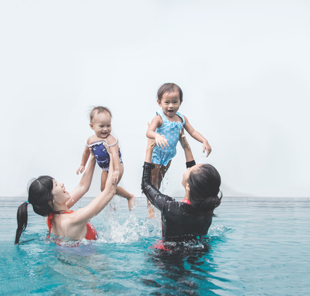two babies having fun in the swimming pool with their motherの写真素材