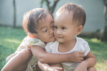 Two cute baby in the park embrace and kissingの写真素材