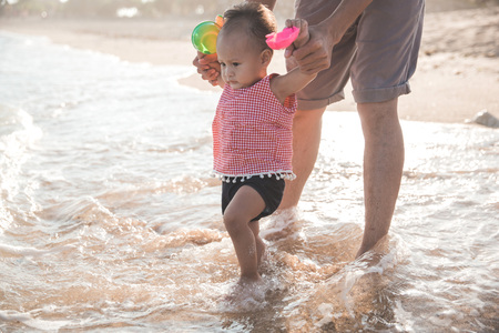 father taking his baby to the beach and have fun with the waterの写真素材